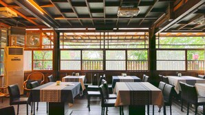 An indoor dining area with multiple tables and chairs, large windows with a view of greenery, and a ceiling with exposed beams and lighting fixtures. - Sakura B&B (Ji'an)