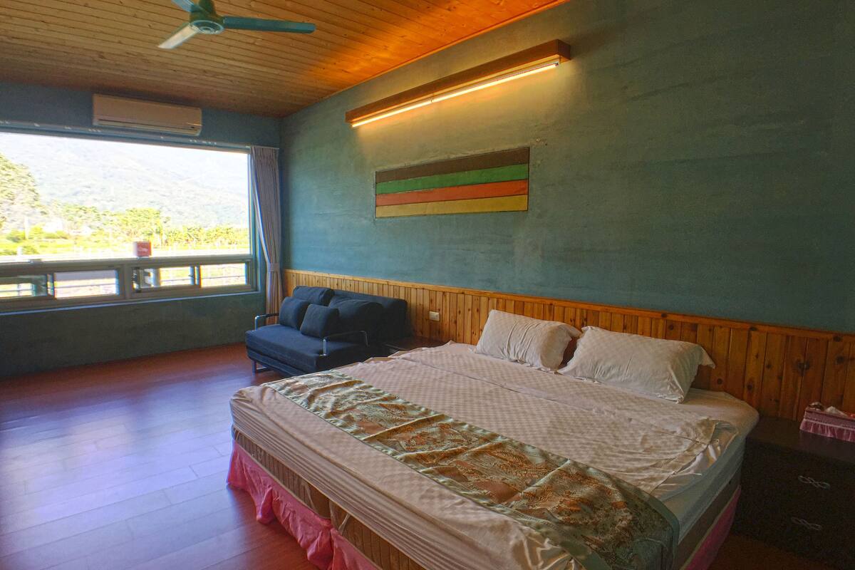 A bedroom with a bed, a window, a ceiling fan, and a wall-mounted light fixture.