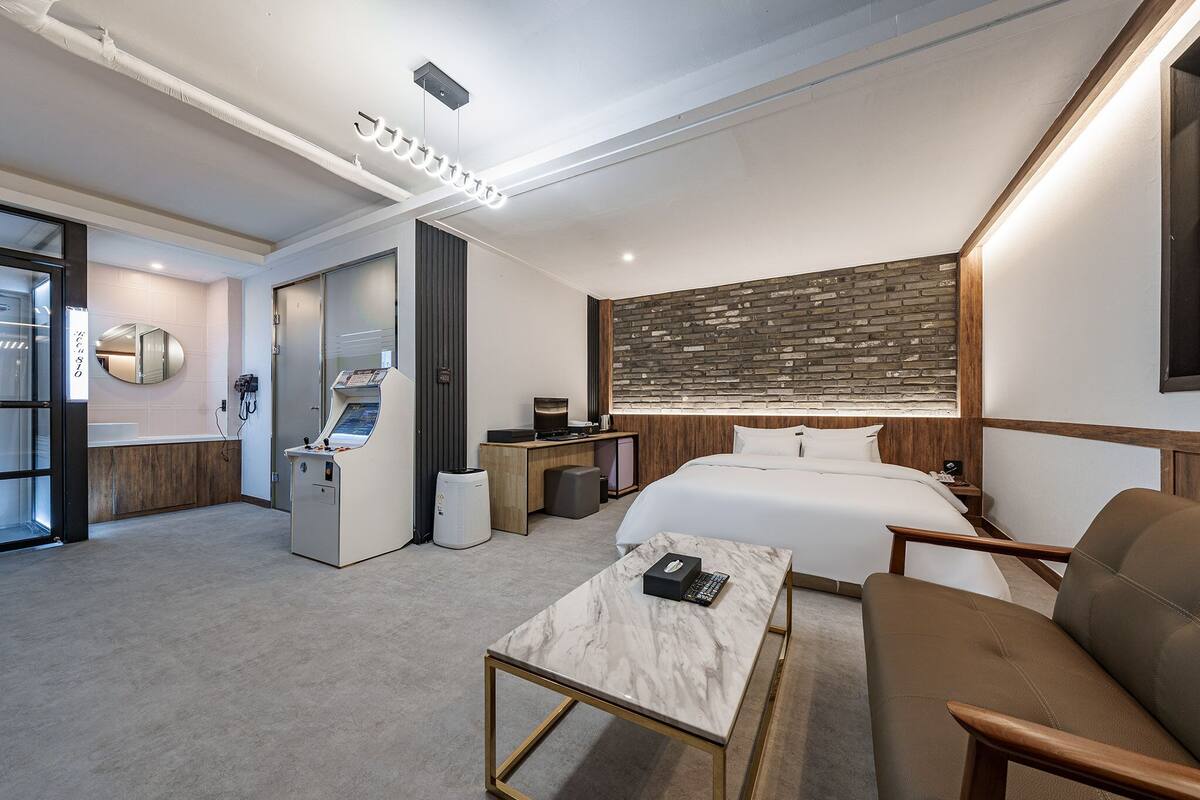 A modern hotel room with a large bed, a desk with a computer, a coffee machine, and a small seating area.