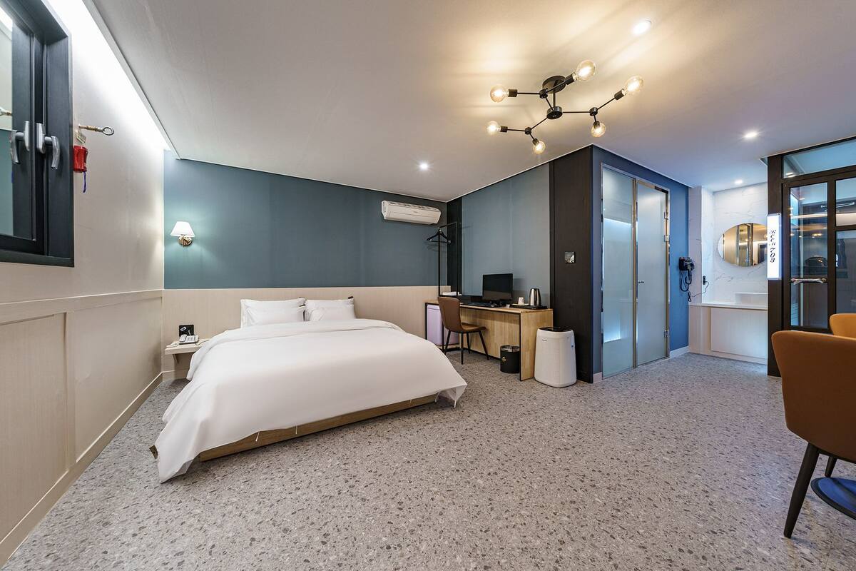A modern hotel room with a large bed, a desk, a chair, and a bathroom visible through an open door.