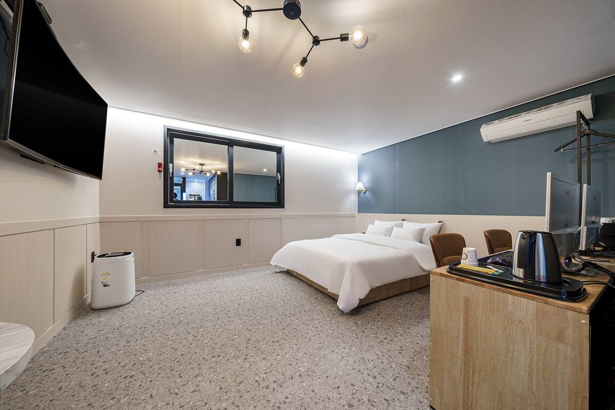 A modern hotel room with a bed, a desk with a coffee maker, a TV, and a window.
