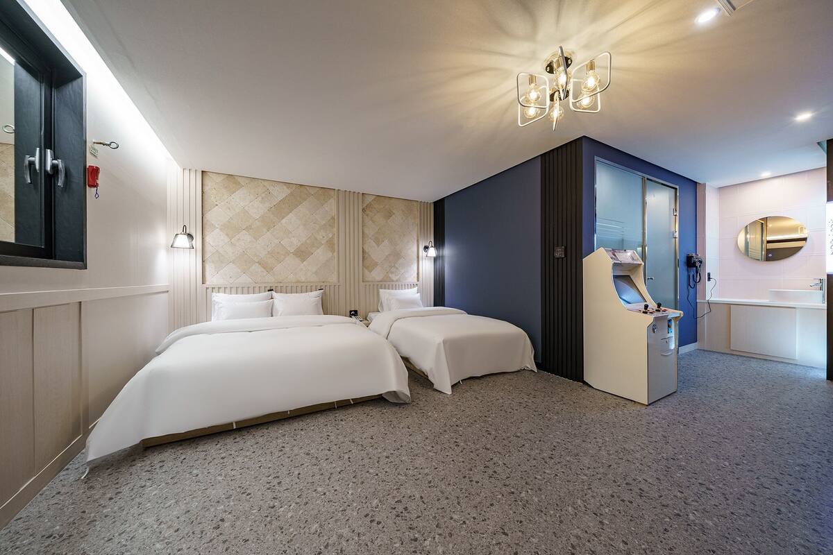 A hotel room with two beds, a minibar, a mirror, and a chandelier.
