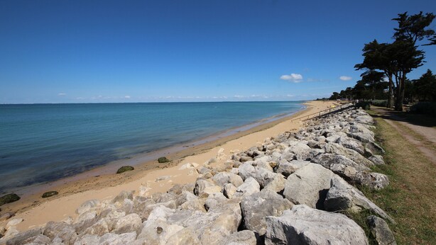 A beach with a rocky shoreline, clear blue water, and a path leading to the beach. - Henriette, between beach and market (La Brée-les-Bains)