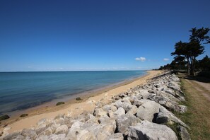 Une plage bordée d’un rivage rocheux, aux eaux d’un bleu limpide, et un sentier qui mène à la plage.