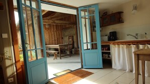A rustic kitchen with wooden walls, a tiled floor, and a blue-framed door leading outside. - Henriette, between beach and market (La Brée-les-Bains)