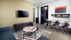 A modern living room with a flat-screen TV, a sofa, a coffee table, and a dining area with chairs. - AFAM Residence (Dammam)