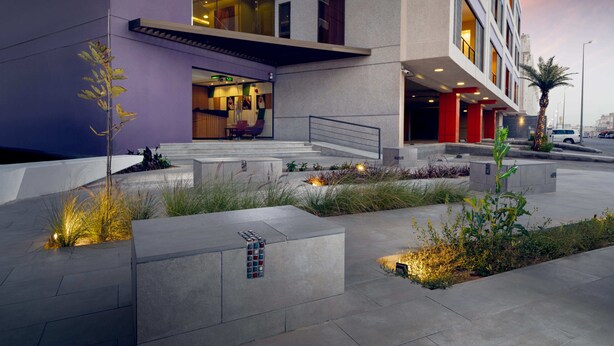 A modern hotel with a purple facade, a well-lit entrance, and a landscaped outdoor area with plants and seating. - AFAM Residence (Dammam)