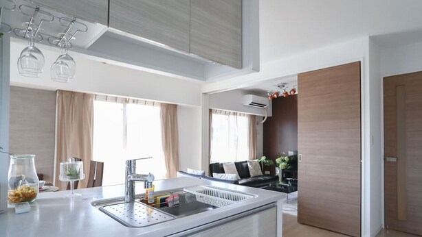 A modern kitchen with a stainless steel sink, a built-in oven, and a dining area with a black sofa.