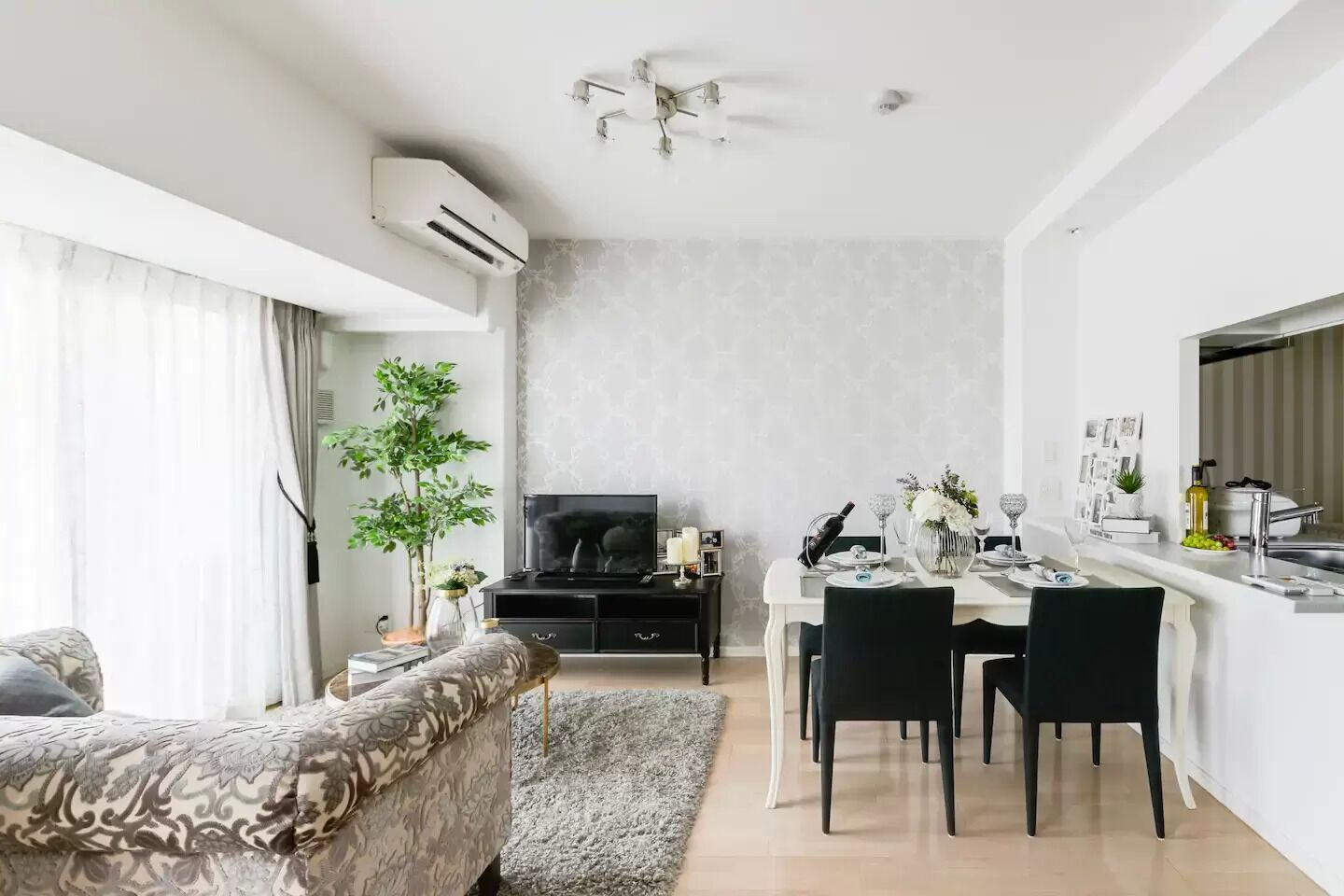 A modern living room with a sofa, a dining area with a table and chairs, a TV, and a kitchen area with a countertop and sink.