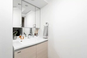 A modern bathroom with a white sink, mirror, and beige cabinets. - Crystal Exe Nipponbashi St35 (Osaka)