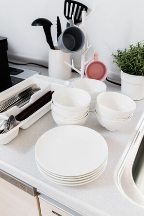 A kitchen counter with stacked white plates, a white tray with utensils, and a potted plant. - Crystal Exe Nipponbashi St36 (Osaka)