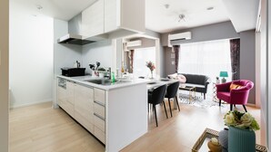 A modern kitchen with white cabinetry, a central island, and a dining area with black chairs. - Crystal Exe Nipponbashi St36 (Osaka)