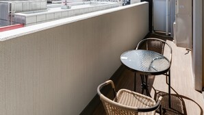 A balcony with a city view, two wicker chairs, and a small round table. - Crystal Exe Nipponbashi St36 (Osaka)
