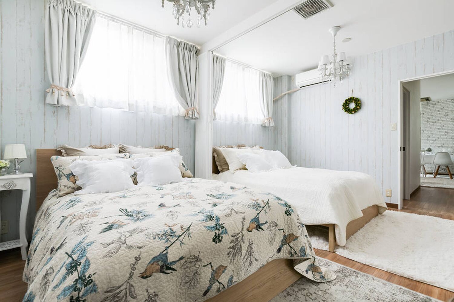 Une chambre avec deux lits, un lustre, un tapis blanc et une porte donnant sur une autre pièce.