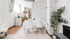 Un salon moderne avec un mur en briques blanches, un coin repas avec une table et des chaises blanches, un canapé blanc et une grande plante en pot.