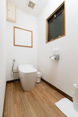 Un baño pequeño y limpio con inodoro, bidé y ventana con marco de madera.