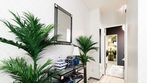 Un couloir avec une console en métal noir sur laquelle sont disposés des objets décoratifs et des plantes, un miroir au-dessus, et une porte donnant sur une autre pièce.