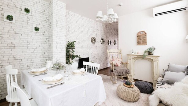 Un espace repas agrémenté d’un mur en briques blanches, d’un lustre, d’une cheminée et d’un coin salon confortable.