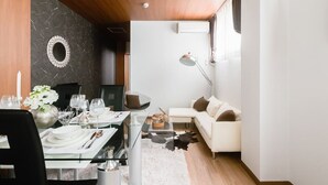 A modern dining area with a wooden ceiling, a round mirror, and a white sofa in a bright room with a large window. - Ota Building St31&32 (Osaka)