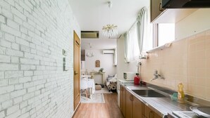 A narrow kitchen with a brick wall, wooden cabinets, a stainless steel sink, and a microwave. - Ota Building St31&32 (Osaka)