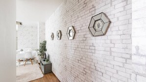 A room with a white brick wall, a dining area with a white table and chairs, and a gray cabinet with a plant. - Ota Building St31&32 (Osaka)