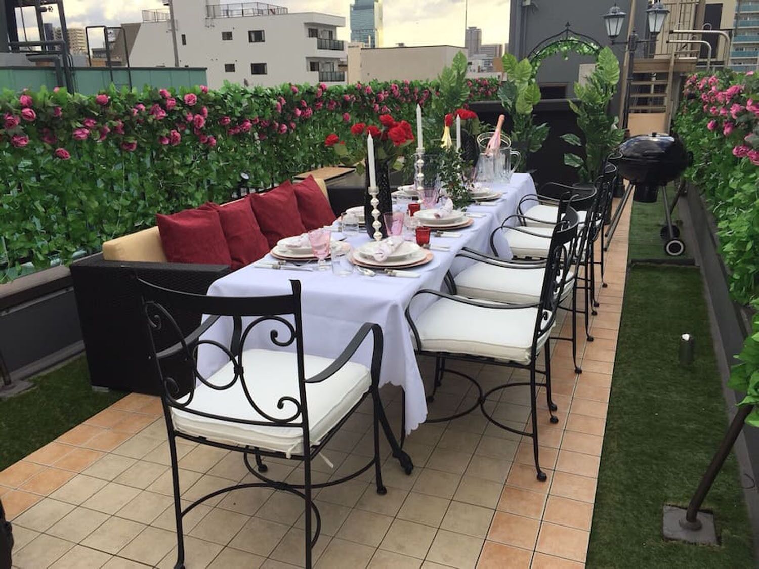 An outdoor dining area with a long table set for a meal, surrounded by chairs and a sofa.