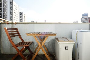 A small balcony with a wooden chair and a table, a white refrigerator, and a cityscape in the background. - Private House St8 (Osaka)