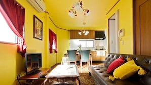 Een woonkamer met een bank, een salontafel en een televisie. In de achtergrond is een keuken met een eethoek te zien.