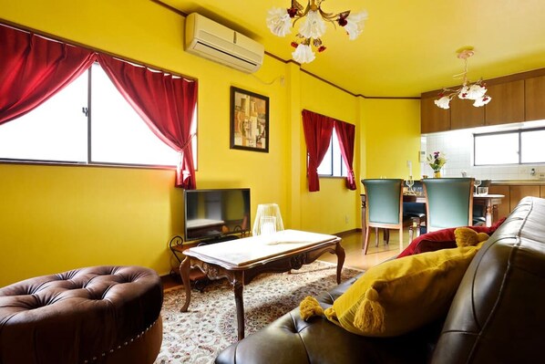 A living room with a TV, a sofa, a coffee table, and a dining area with a chair and table. - Private House St8 (Osaka)