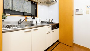 A kitchen with a stainless steel sink, white cabinets, a window with a floral curtain, and a wooden door. - Lumiere Higashi Shinsaibashi St27 (Osaka)