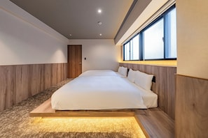 A modern bedroom with a large bed, wooden paneling, and a window with blinds.