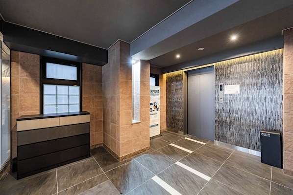 A modern elevator area with a digital display, a fire extinguisher, and a sign for airport transfer service.