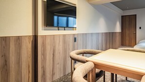 Ein Hotelzimmer mit Holzwand, einem an der Wand befestigten Fernseher, einem Bett mit weißer Bettwäsche und einem kleinen Tisch mit Stühlen.