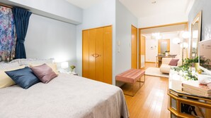 A bedroom with a bed, bedside table, and a bench. There is a wooden wardrobe, a mirror, and a dining area in the background. - Lumiere Higashi Shinsaibashi St27 (Osaka)