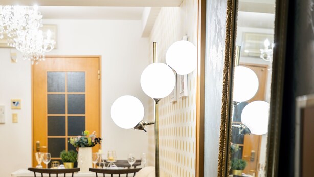 A cozy living room with a sofa, a dining area with a table and chairs, and a large mirror with lights. - Lumiere Higashi Shinsaibashi St27 (Osaka)