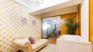 A room with a polka dot wallpaper, a beige sofa, a white crib, and a mirror reflecting a bathroom. - Lumiere Higashi Shinsaibashi St27 (Osaka)