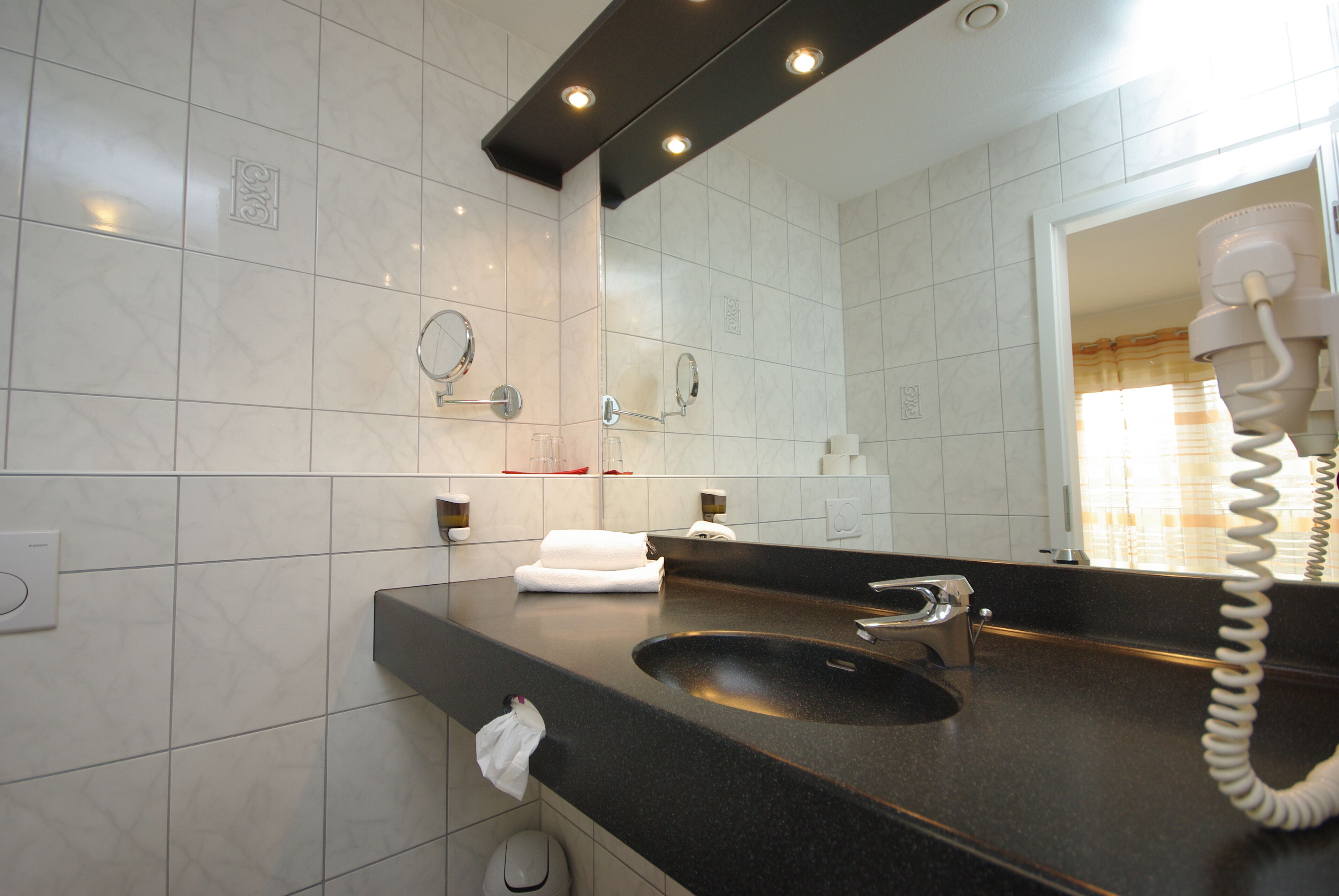 A modern bathroom with a black sink, a large mirror, and a hairdryer on the counter.