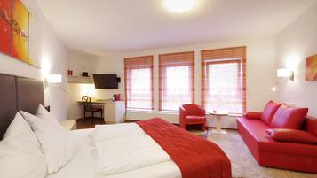 A hotel room with a bed, a red sofa, a desk with a chair, and a TV.