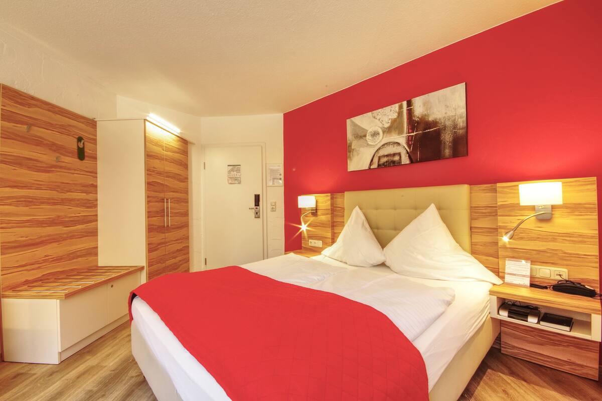 Quarto de hotel com cama, guarda-roupa, mesa de cabeceira e uma obra de arte na parede.
