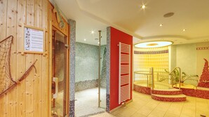 A spa area with a wooden wall, a glass door leading to a shower, and a red wall with a tiled bench. - Hotel Jakob (Gross-Umstadt)
