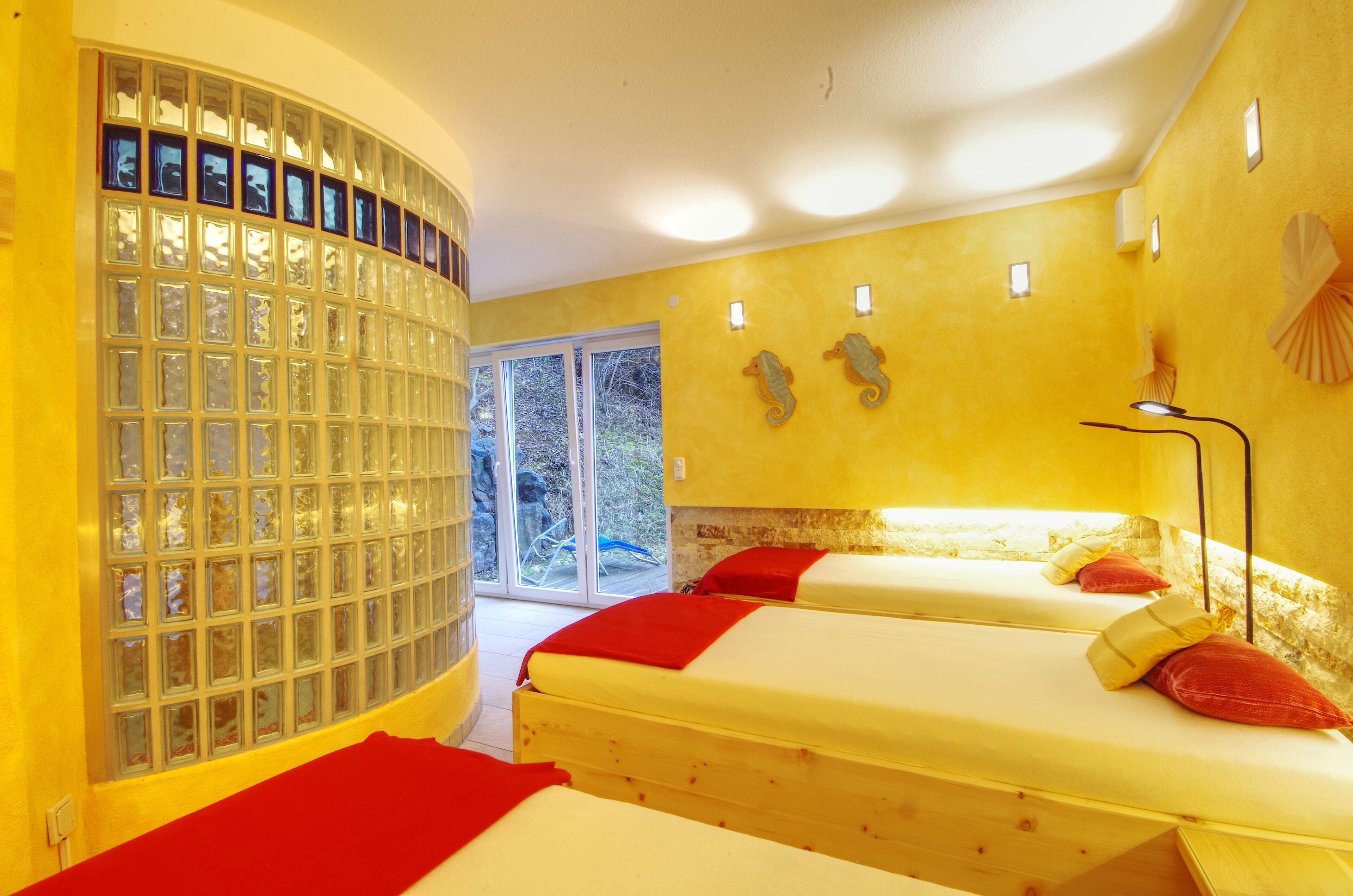 A room with two beds, a glass block wall, and a view of the outdoors.