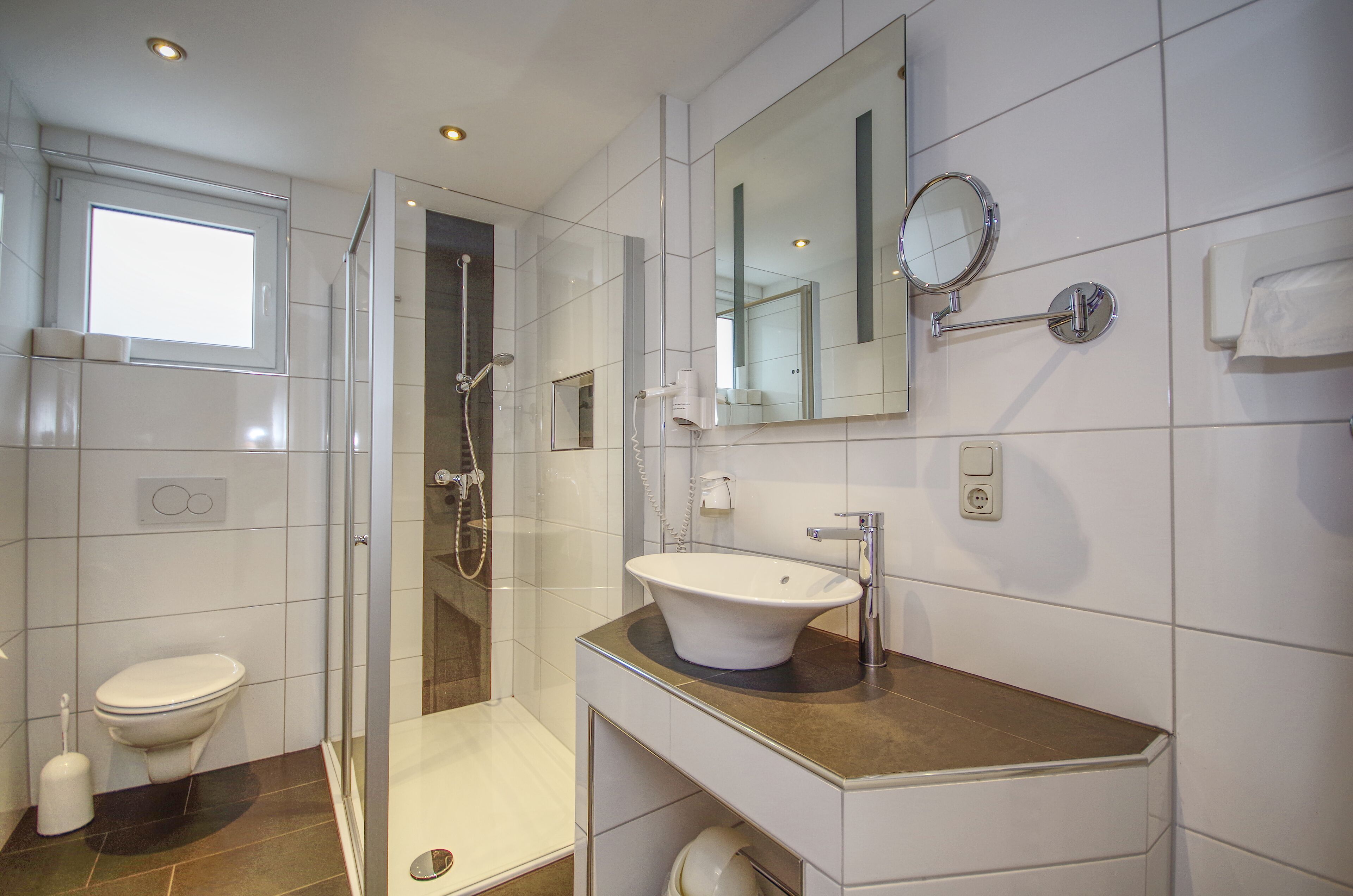 A modern bathroom with a glass-enclosed shower, a white sink, and a large mirror.