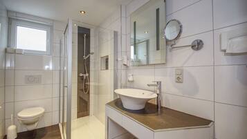 A modern bathroom with a glass-enclosed shower, a white sink, and a large mirror.