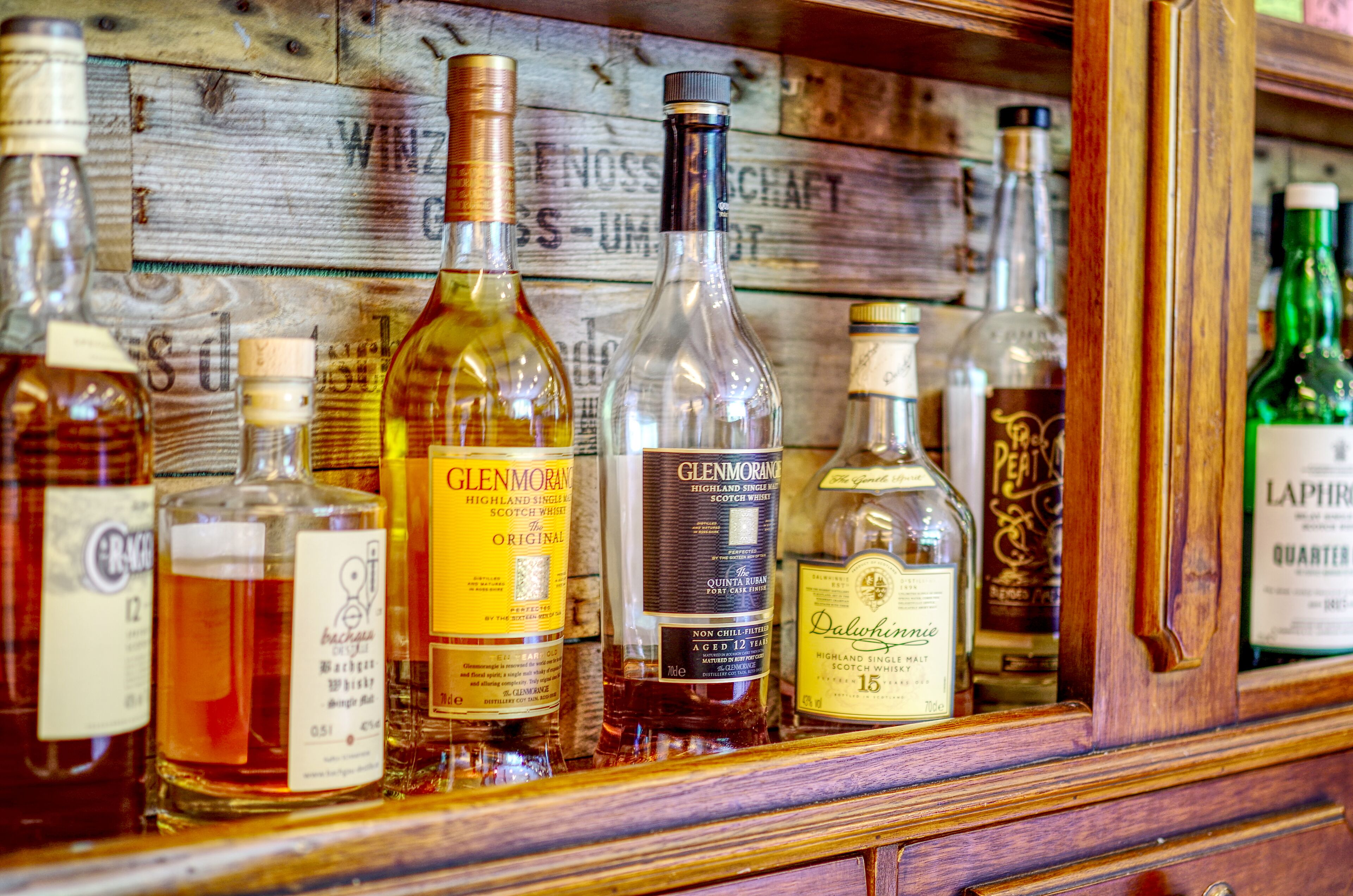 Variedad de botellas de whisky exhibidas sobre una estantería de madera.