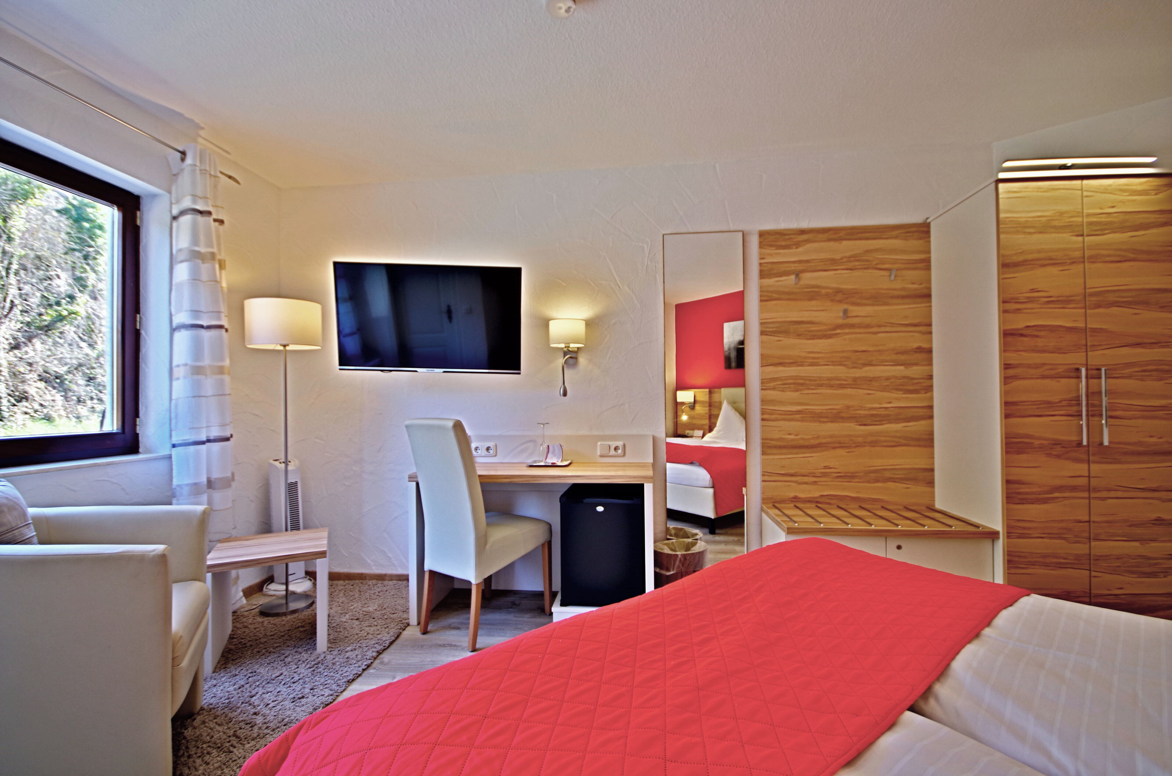 Habitación de hotel con cama, escritorio, silla, televisor, armario y ventana.