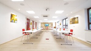 A conference room with white tables and red chairs, a stone wall, and artwork on the walls. - Hotel Jakob (Gross-Umstadt)