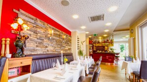 A restaurant with a red accent wall, wooden paneling, and a bar area. Tables are set with white tablecloths and candles. - Hotel Jakob (Gross-Umstadt)