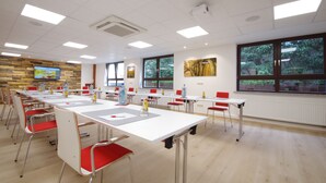 A conference room with long tables, red chairs, and a large window with a view of trees. - Hotel Jakob (Gross-Umstadt)