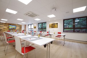 A conference room with long tables, red chairs, and a large window with a view of trees.
