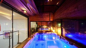 A modern spa area with multiple hot tubs illuminated by blue lighting, a glass partition, and a wooden interior. - Vista Hill Pool Villa (Gapyeong)